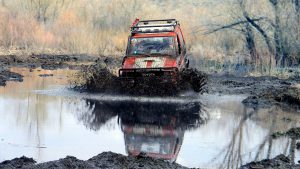 Красный джип Тойота пробирается вброд по болотистой местности