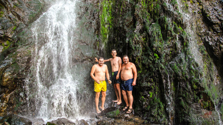 Туристы под холодными струями водопада