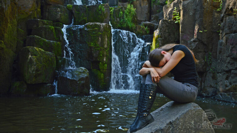 Девушка-модель на камне у подножья водопада
